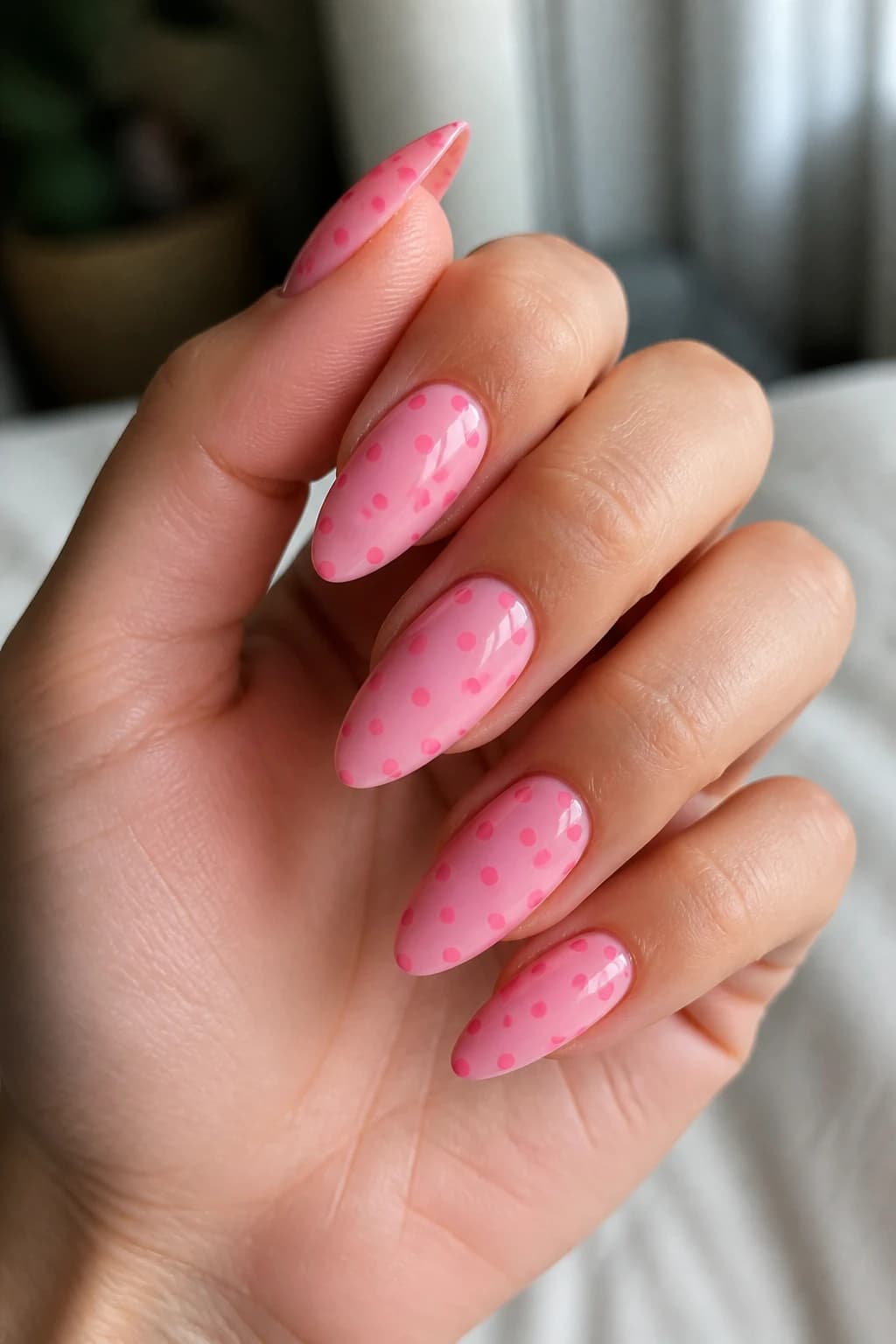 Long almond nails in pink with a polka dot design and a glossy finish