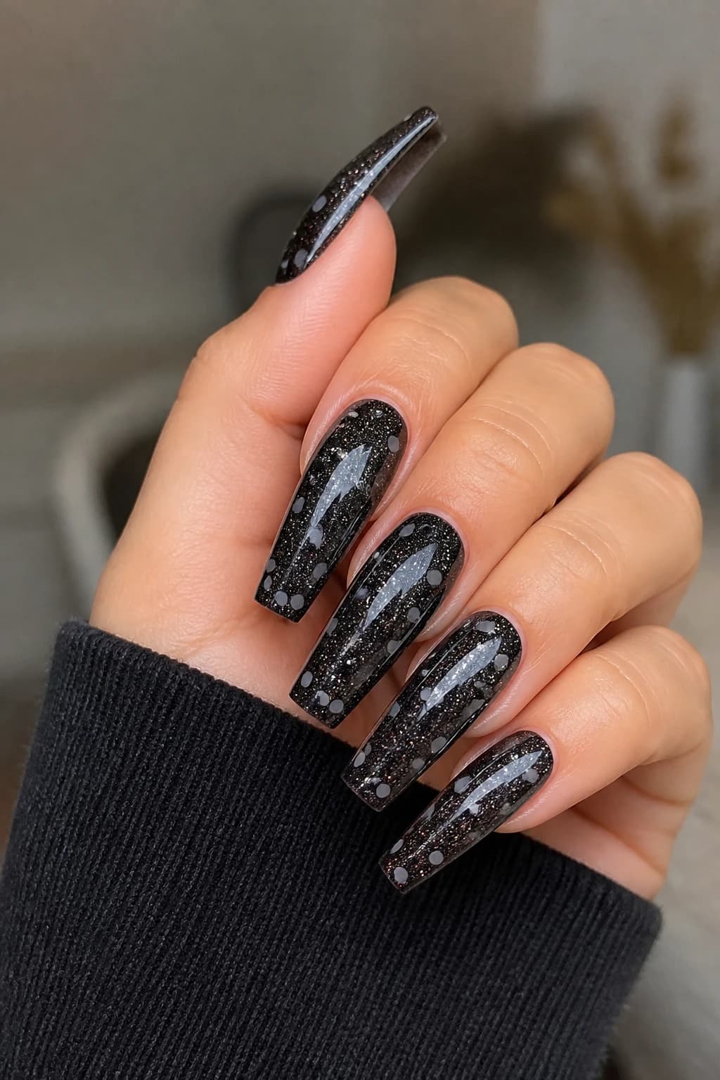 Long coffin nails in black with a polka dot design and a glitter finish
